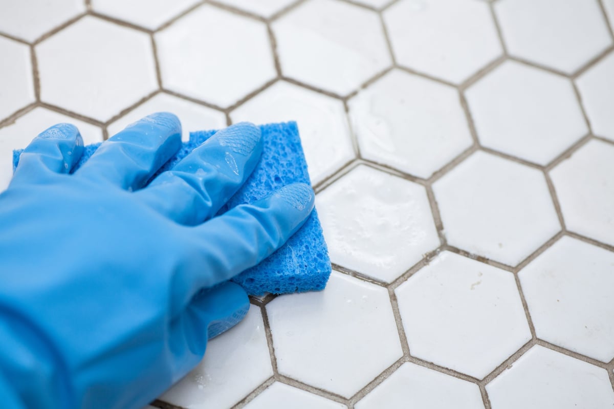 Person in blue gloves holding a sponge cleaning a white tile floor